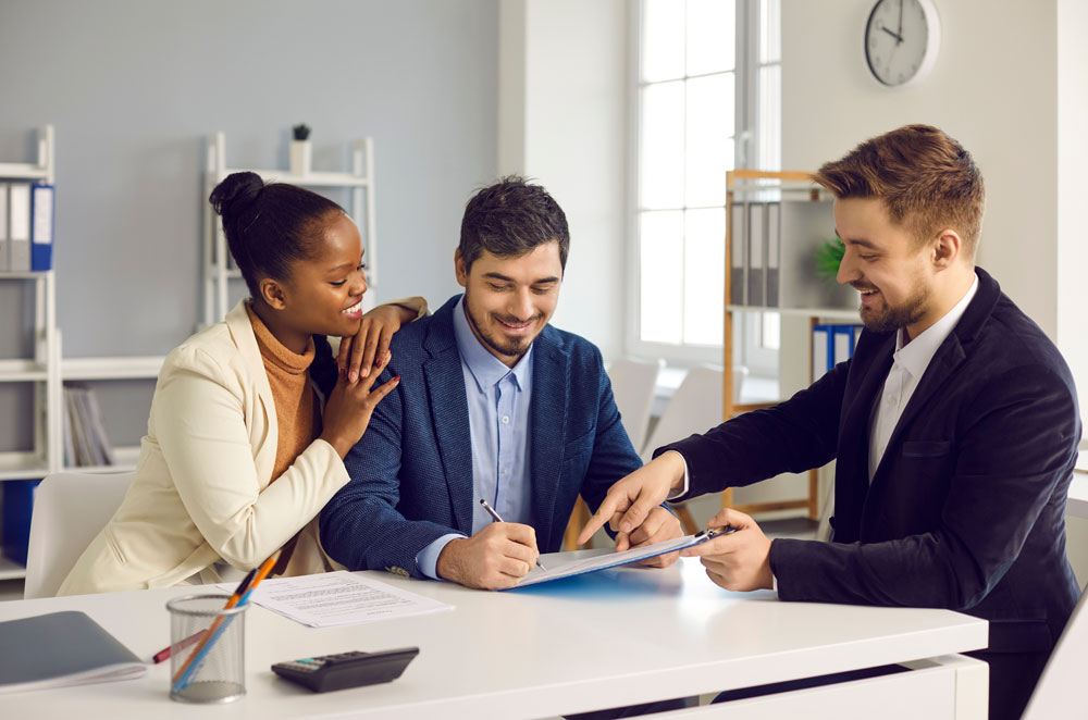 Successful-meeting-with-broker-bank-agent-insurer.-Happy-mixed-ethnicity-couple-customers-sign-mortgage-loan-contract.-Smiling-african-ameri